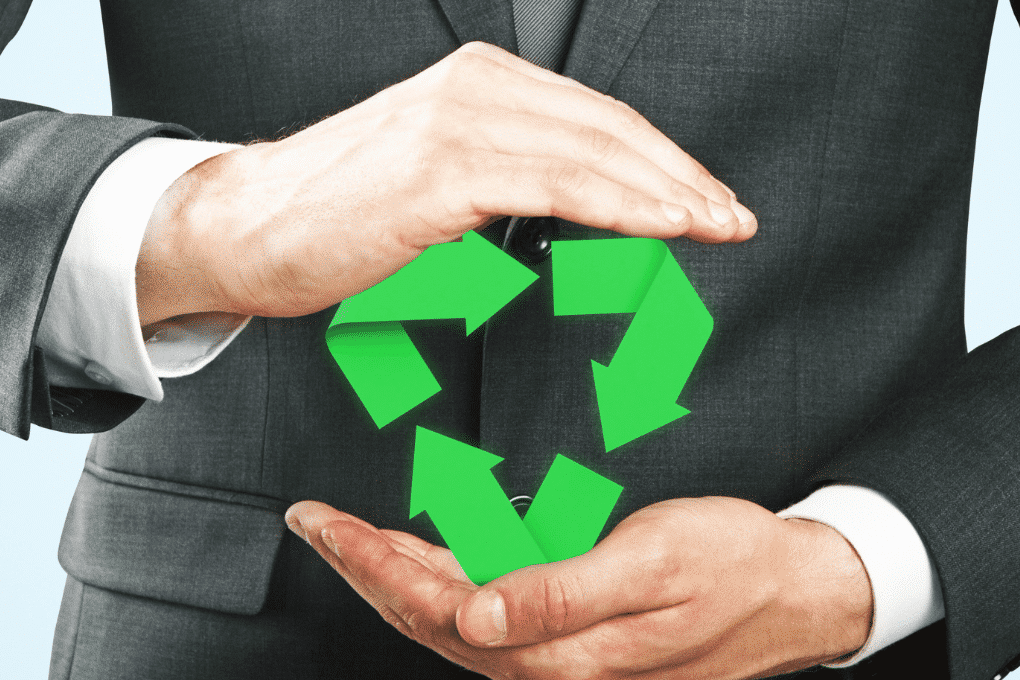mężczyzna ubrany w garnitur trzyma w dłoniach zielony znak recyklingu